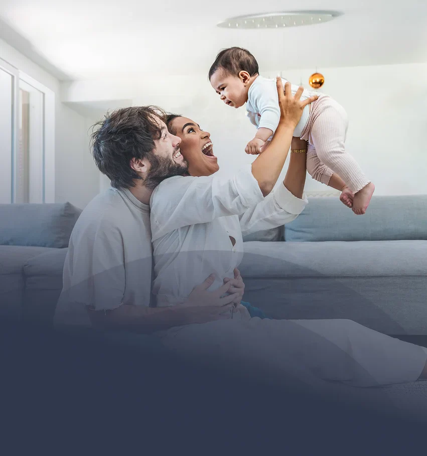 A joyful moment of a parent lifting their baby playfully in a cozy living room, with soft furnishings and warm lighting.