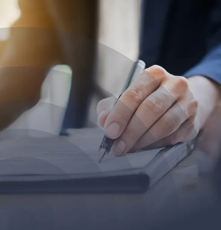 A close-up of a person's hand writing notes in a notebook with a pen, suggesting focus and productivity in a professional setting.